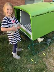 A little girl holding a chicken outside an Eglu.