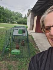 A selfie of a woman next to her chickens in the Eglu cube chicken coop.