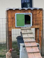 A green autodoor attached to a wooden chicken coop.