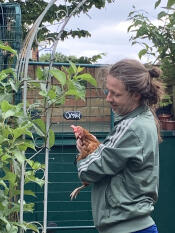 A person holding a chicken next to the walk in run.