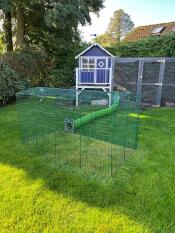 A green tunnel in a garden connecting a rabbit enclosure and a rabbit hutch