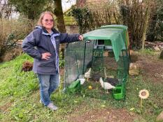 A person standing next to the green Eglu Cube chicken run set up with chickens inside.