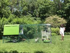 a young girl in a garden with a green cube chicken coop and a run attached