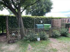 A large eglu cube with a run and cover inside a small fenced side of a garden