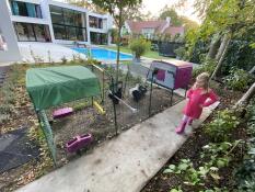 a girl stood next to a large cube chicken coop with a run and cover in a city garden