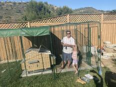 A man standing inside an Omlet walk in chicken run with a plastic chicken coop inside.