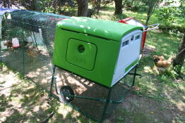 The green Eglu Cube chicken coop with wheels and a run set up in a garden.
