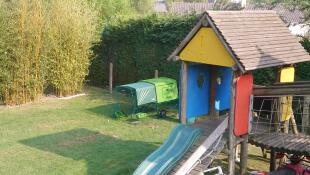 a cube chicken coop with a run and cover in a garden with a climbing frame